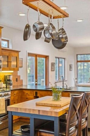 A modern kitchen with hanging pots, wooden cabinets, and a large window.
