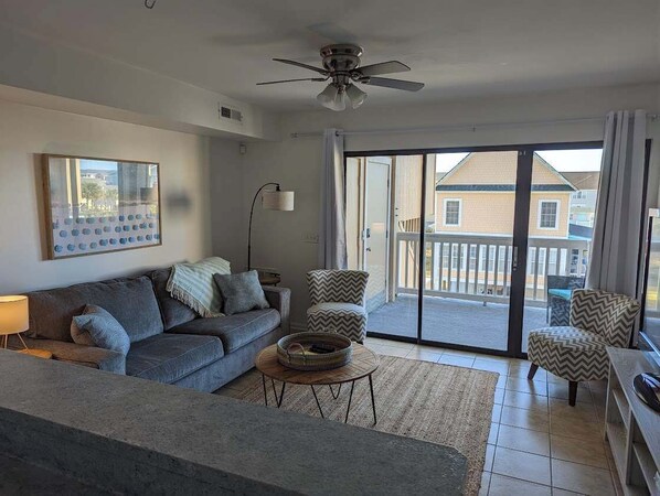 A living room with a sofa, a coffee table, a ceiling fan, and a view through a sliding glass door to the outside.