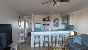 Un salon comprenant un téléviseur, un canapé, une table basse et un coin cuisine avec un tabouret de bar.