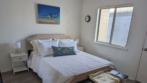 Une chambre à coucher avec un lit, des tables de chevet, une commode, une fenêtre avec des stores et un tableau au mur.