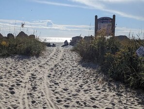A sandy beach path leading to a signpost with text, surrounded by vegetation.