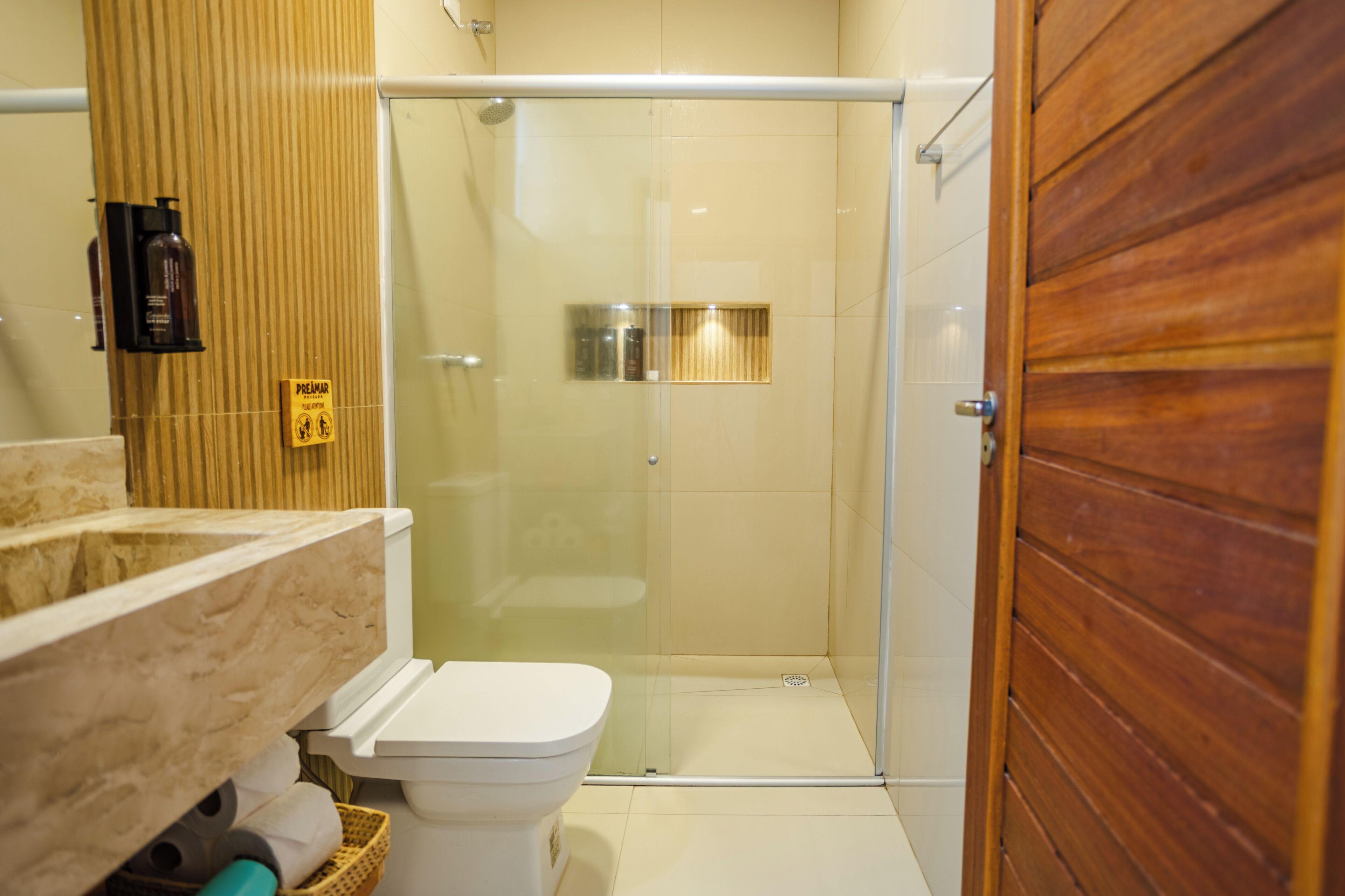 Un bagno con cabina doccia in vetro, un water e una porta in legno.