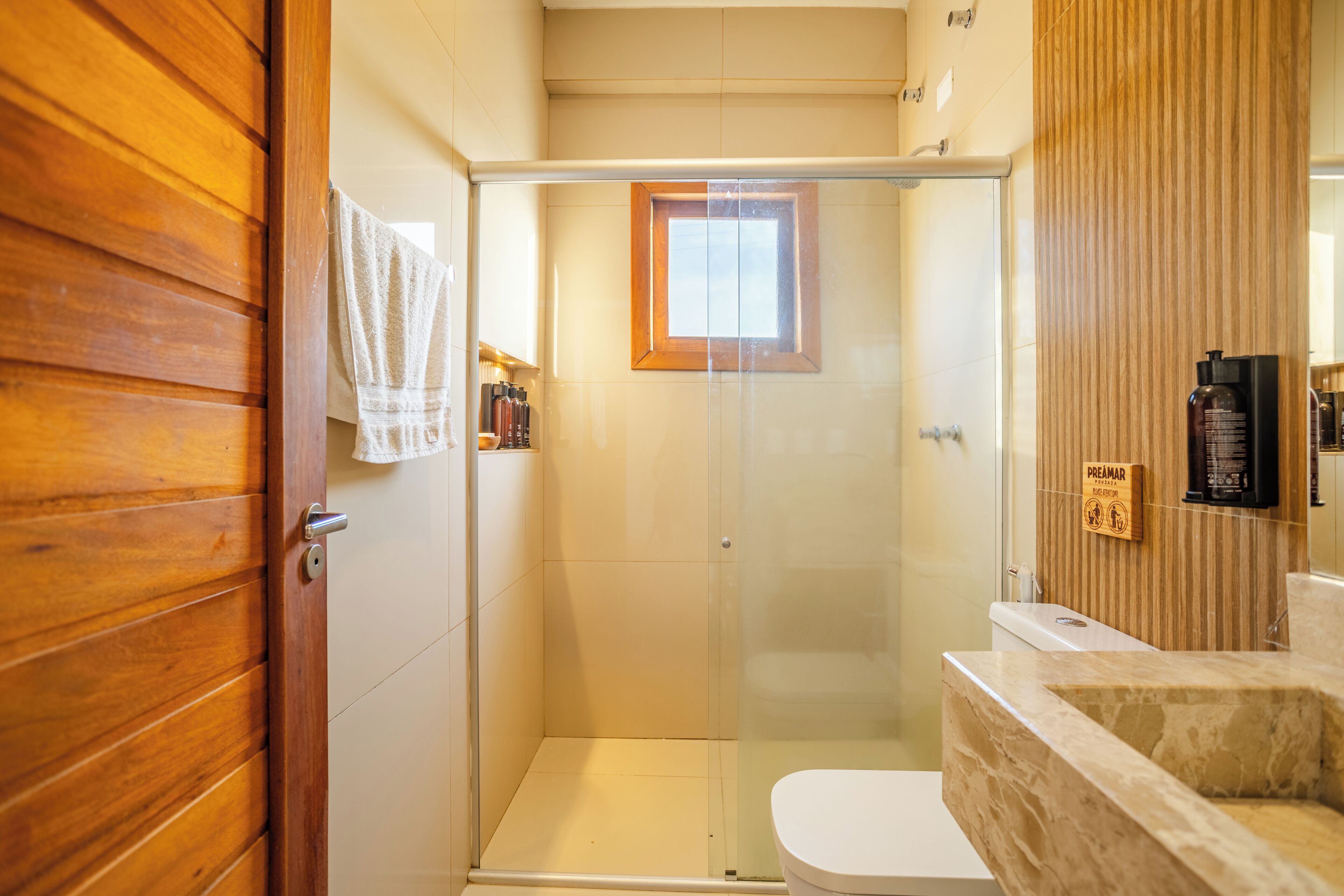 A bathroom with a glass-enclosed shower, a wooden door, a white toilet, and a marble sink.