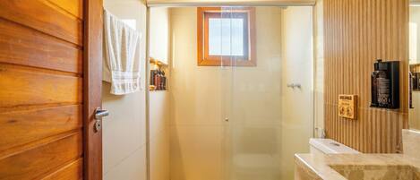 A bathroom with a glass-enclosed shower, a wooden door, a white toilet, and a marble sink.