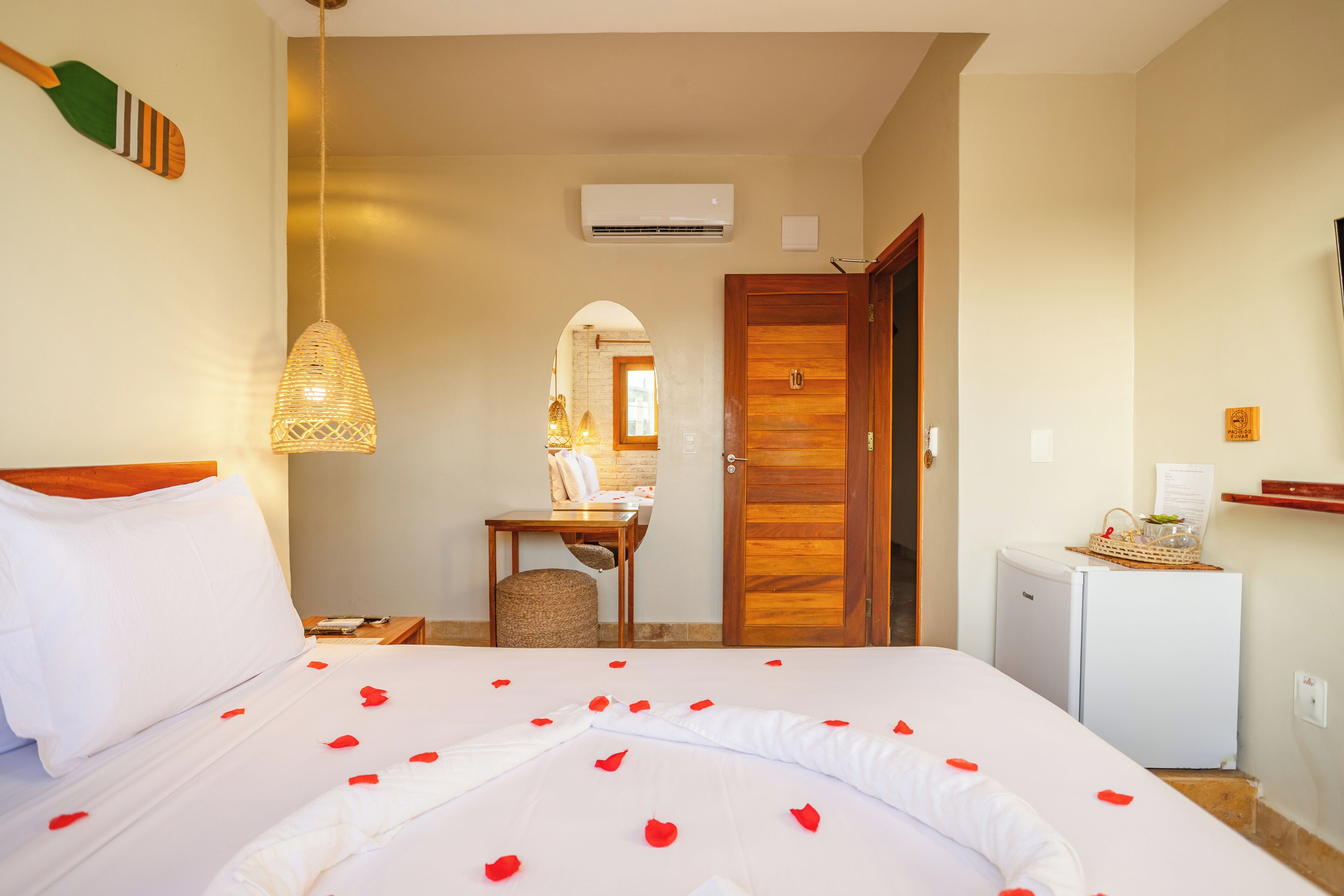 A hotel room with a bed, a desk, a chair, a refrigerator, and an air conditioning unit.