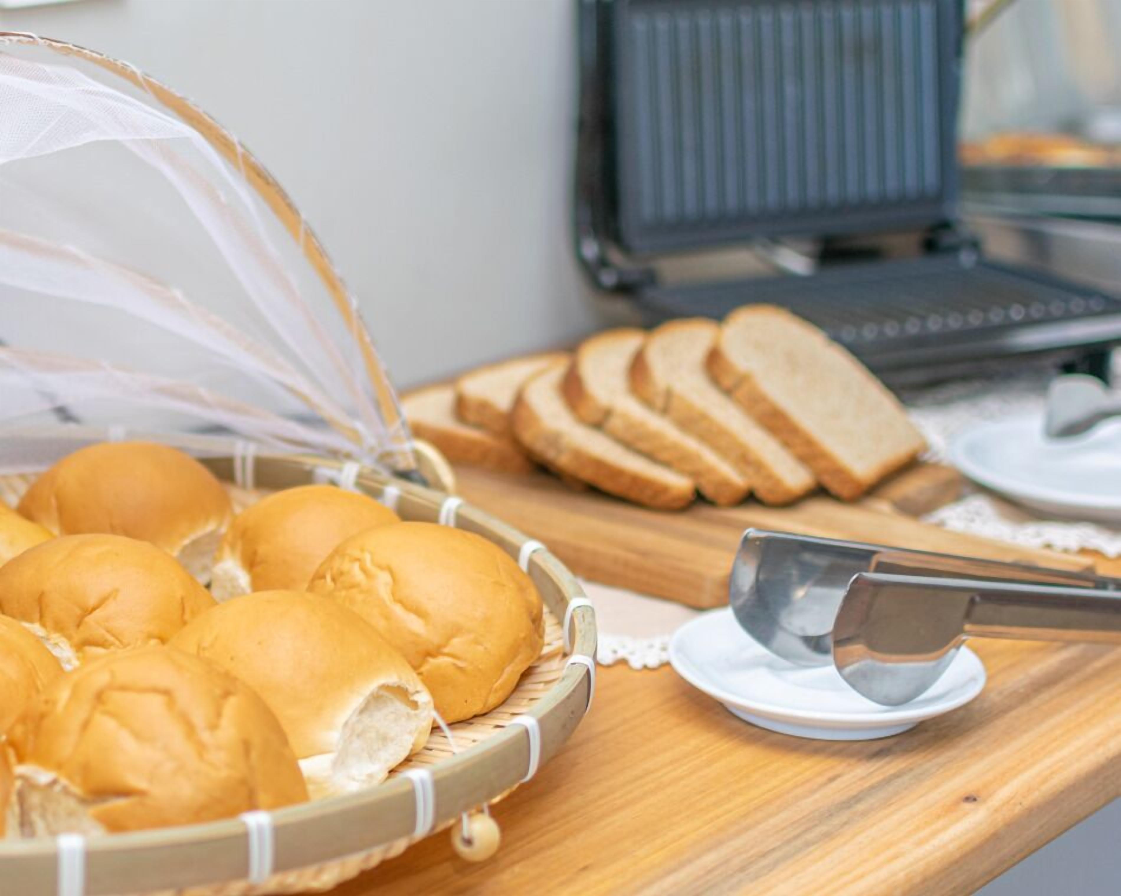 Een ontbijtbuffet met broodjes en sneetjes brood op een houten tafel.