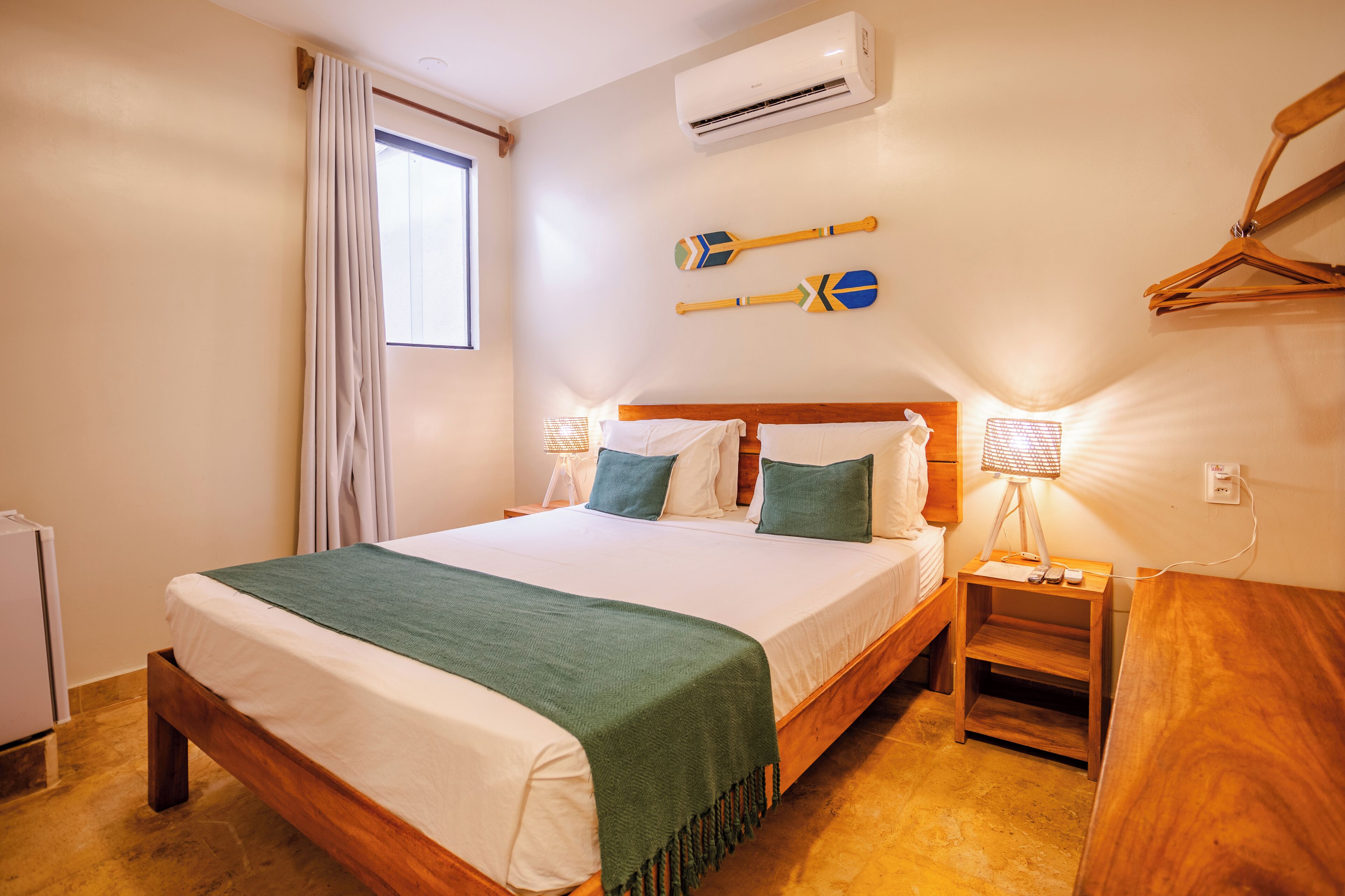 A neatly made bed with a green blanket, a bedside lamp, and two decorative paddles on the wall.