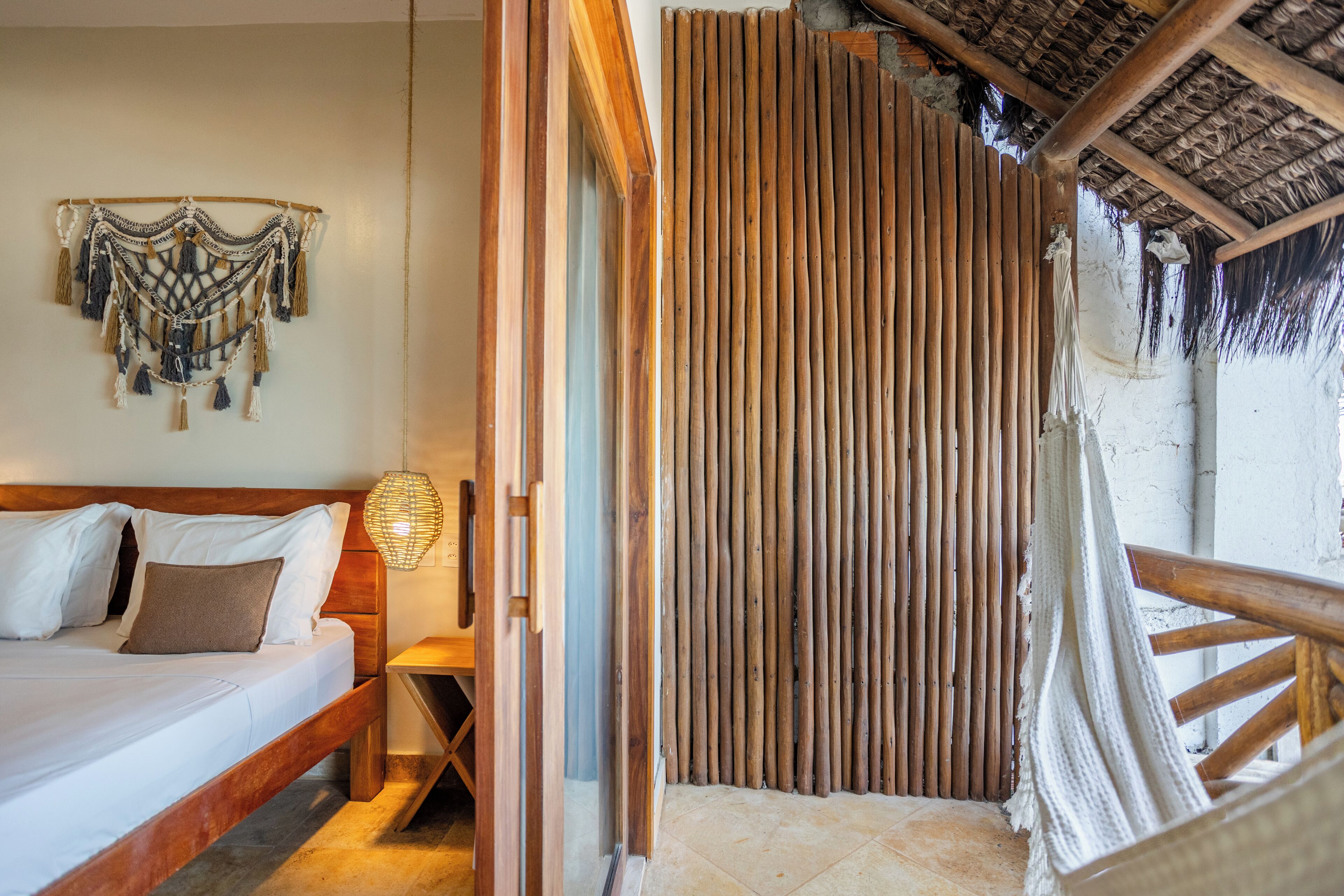 A room with a bed, wooden headboard, a woven wall hanging, and a bamboo partition.