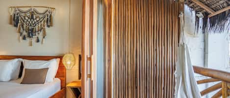 A room with a bed, wooden headboard, a woven wall hanging, and a bamboo partition.