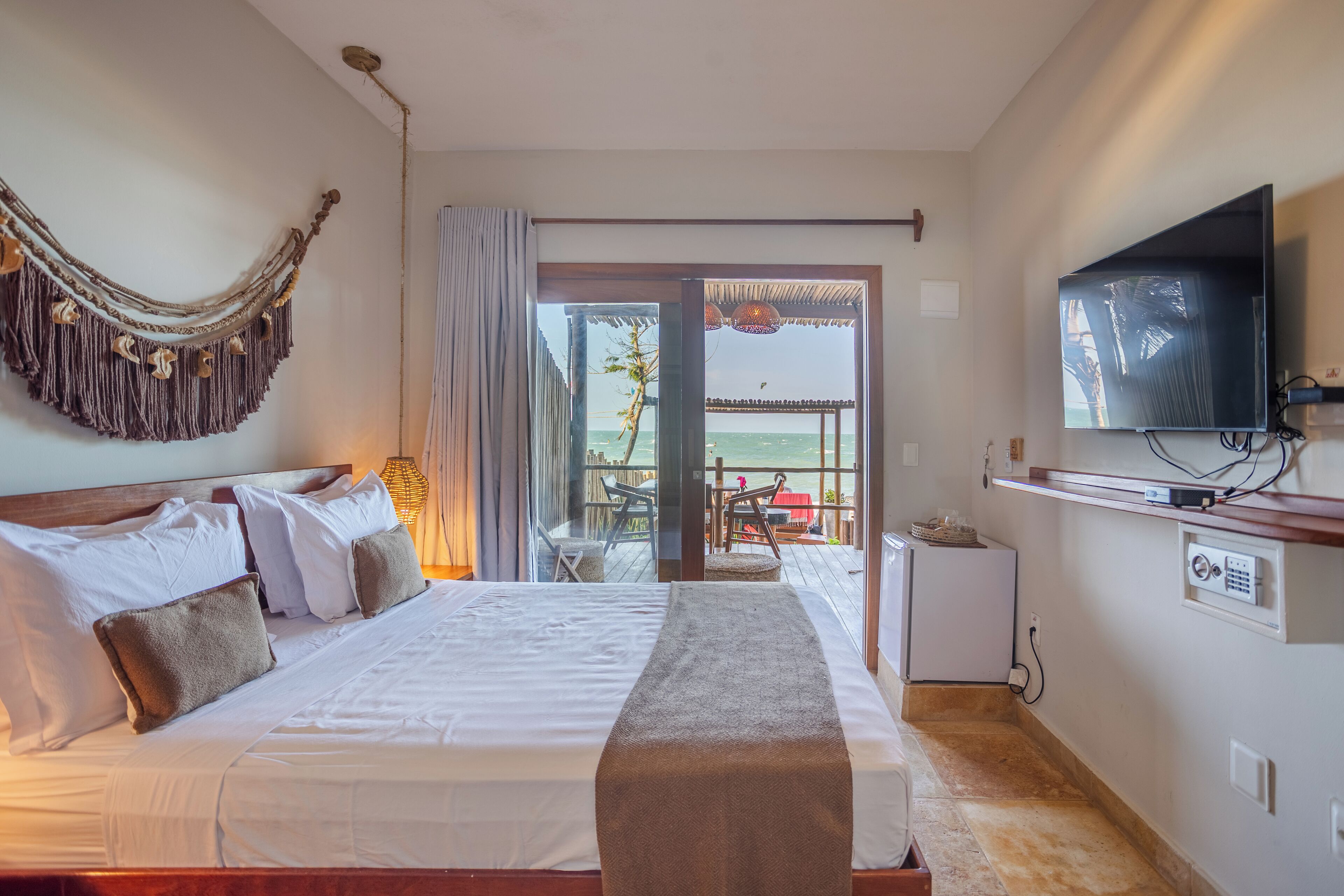 A hotel room with a bed, a TV, a balcony with a table and chairs, and a view of the sea.