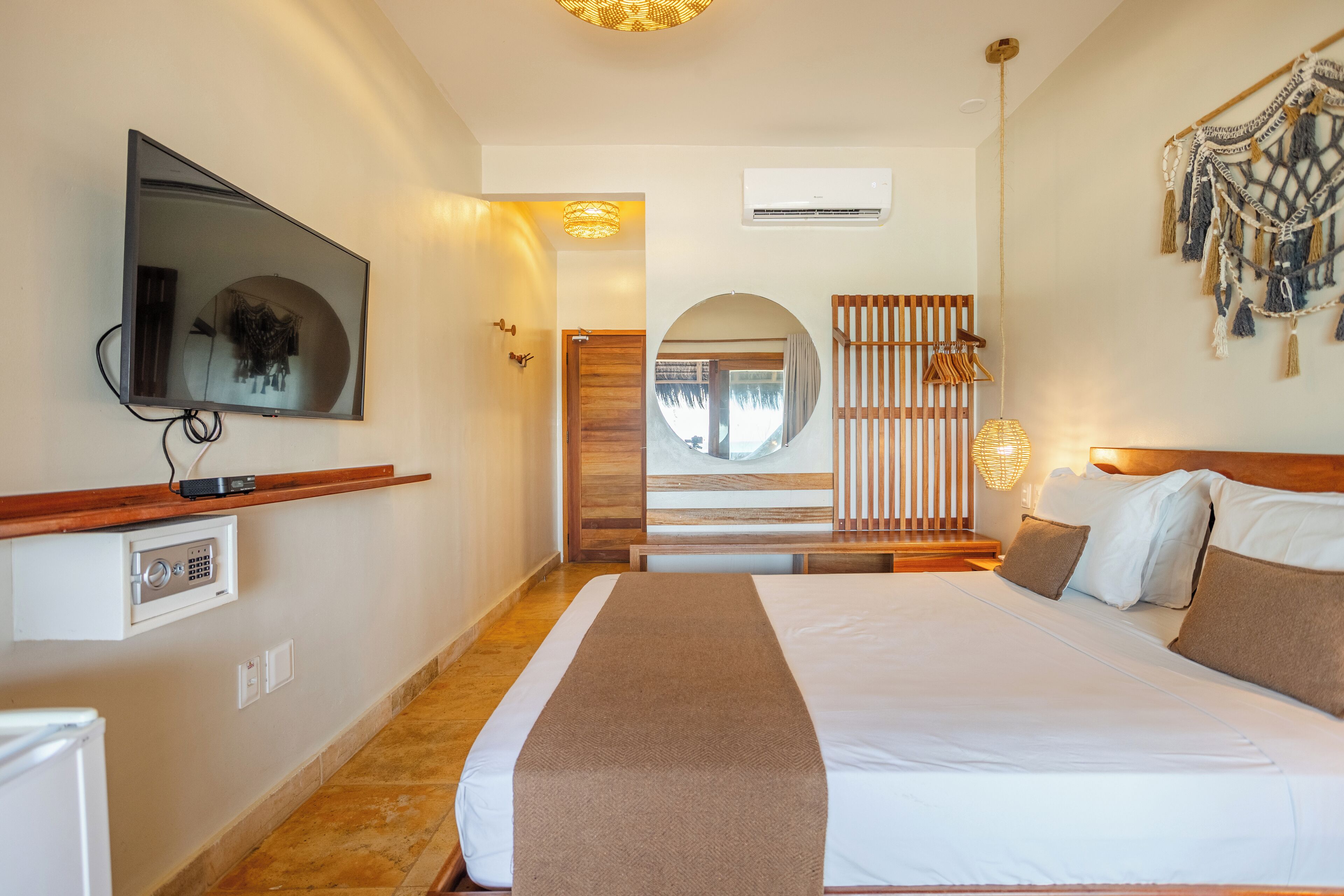 Una habitación de hotel con una cama grande, un televisor montado en la pared, un cabecero de madera y un adorno decorativo de macramé en la pared.