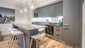 A modern kitchen with grey cabinets, a central island with bar stools, pendant lighting, and a microwave. - Lapia104 : Splendid one bedroom + cabin (MORZINE)