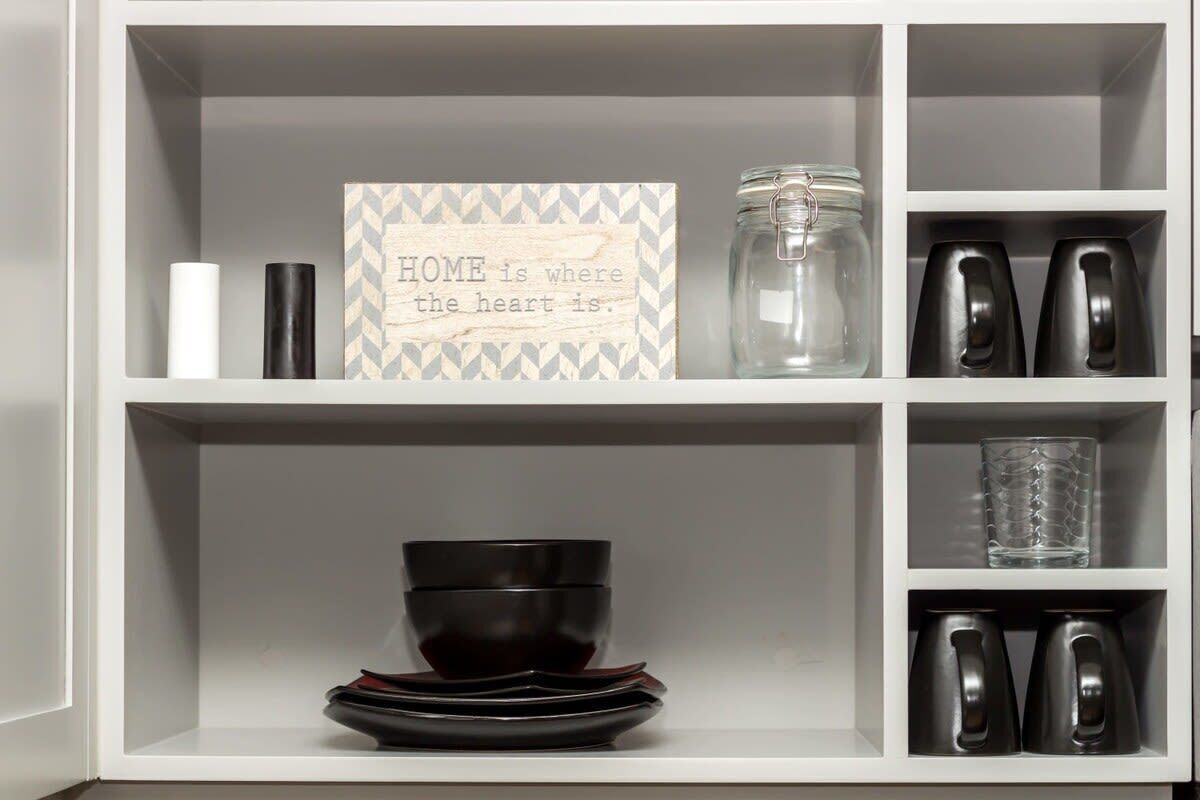 A kitchen shelf with a jar, a candle, a decorative sign, and kitchen utensils.