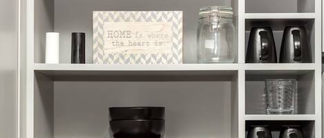 A kitchen shelf with a jar, a candle, a decorative sign, and kitchen utensils.
