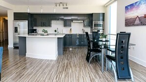 A modern kitchen with a central island, stainless steel appliances, and a dining area with a glass table and chairs. - Charlotte Uptown Fully Furnished Apartments (Charlotte)
