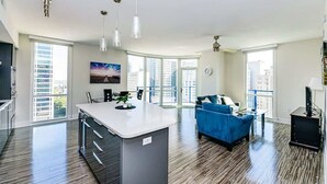 A spacious living area with a central island, a blue sofa, and large windows offering city views. - Charlotte Uptown Fully Furnished Apartments (Charlotte)