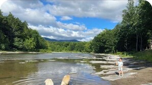 Une rivière aux eaux claires, bordée d’une forêt dense et avec des montagnes en toile de fond.