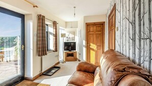 A living room with a leather sofa, a television, and a view of the outdoors. - Juice Trump - UK36670 (Belchford)