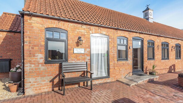 A brick building with a tiled roof, a bench, and a sign reading "Juice Trump Cottage." - Juice Trump - UK36670 (Belchford)