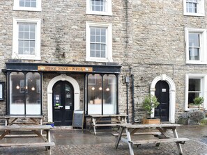 A stone building with a sign reading "The Bake-Well" and a black door. There are picnic tables outside.