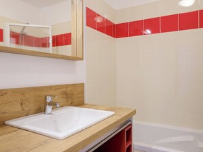 Une salle de bain avec un meuble-lavabo en bois, un lavabo blanc, un miroir et une zone de douche carrelée de carreaux rouges.