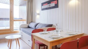 Une pièce moderne avec une table à manger en bois, des chaises rouges, un canapé gris et un mur blanc orné d’un tableau encadré.