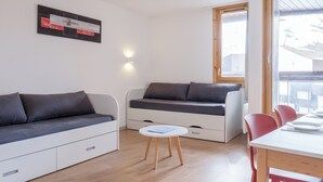 Un espace de vie moderne et compact comprenant un canapé, une petite table et un coin repas avec des chaises.