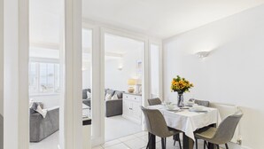 Un comedor con una mesa preparada para dos, un florero con flores amarillas y vistas a una sala de estar con sofá y aparador.