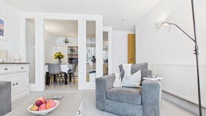 Una sala de estar moderna con un sofá gris, un comedor con mesa y sillas, y una cocina visible a través de una puerta abierta.