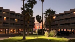 A multi-story hotel with a grassy courtyard, palm trees, and a clear sky. - Lovely, beach view condo (Corpus Christi)