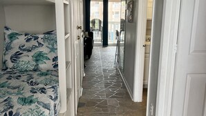 A narrow hallway with a stone-tiled floor, white walls, and a bed with floral bedding. - Lovely, beach view condo (Corpus Christi)