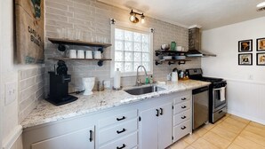 Una cocina con armarios blancos, encimera de granito, cafetera y estufa.