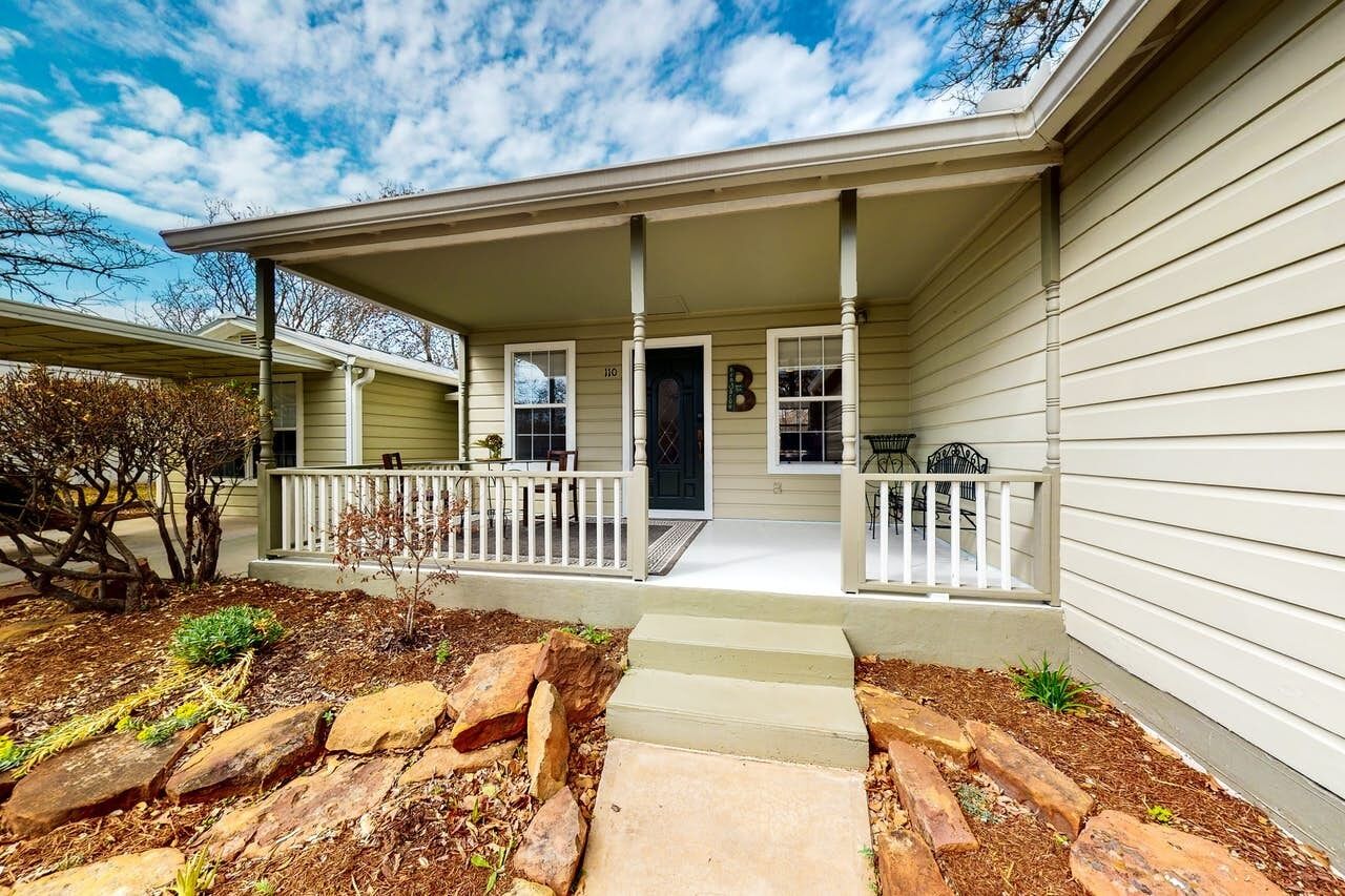 A single-story house with a covered porch, a front door, and a small garden area with rocks and mulch.