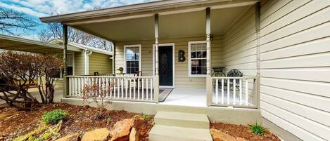 A single-story house with a covered porch, a front door, and a small garden area with rocks and mulch.