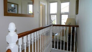 Eine Treppe mit weißen Balustraden und Holzhandläufen, die zu einem Raum mit einem großen Fenster und einem Sessel führt.