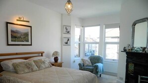 Ein Schlafzimmer mit einem großen Bett, einem Sessel, einem Kamin und einem Fenster mit Blick auf Gebäude.