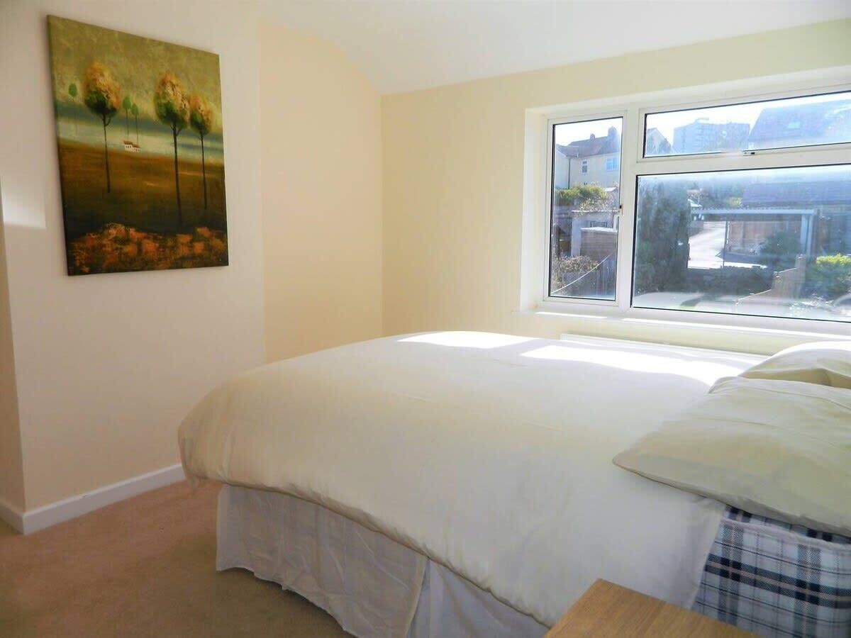 A bedroom with a bed, a window, and a painting on the wall.