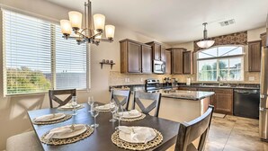 Un comedor con una mesa de madera oscura dispuesta para cuatro personas, rodeada de sillas, y una cocina al fondo.