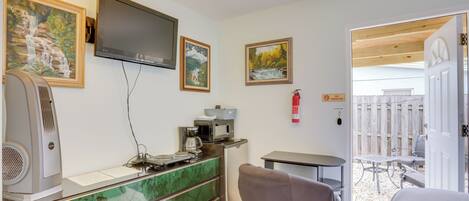 A modern kitchen with a built-in microwave, coffee maker, and a refrigerator. There is a dining area with a table and chairs, and a painting on the wall.