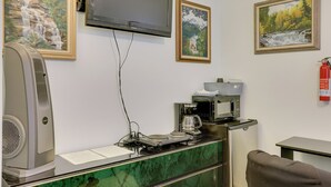 A room with a flat-screen TV, a desktop computer, a coffee machine, and framed paintings on the wall. - Pet-Friendly Stuart Studio < 3 Mi to Downtown! (Stuart)
