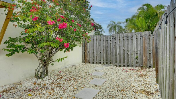 A garden with a wooden fence, a tree with pink flowers, and stepping stones on a gravel path. - Pet-Friendly Stuart Studio < 3 Mi to Downtown! (Stuart)