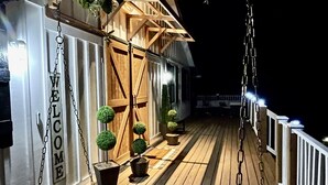 Ett trädäck med en gungstol, en liten träkonstruktion med planterade blommor och en skylt med texten ”VÄLKOMMEN”.