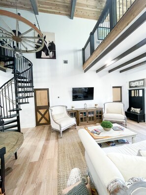 A spacious living area with a staircase, a television, and a large window.