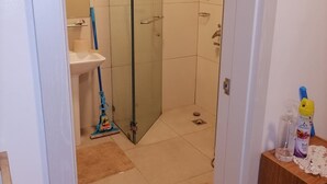 Casa de banho com cabine de duche em vidro, lavatório e esfregão no chão.