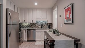 A modern kitchen with white cabinets, stainless steel appliances, a herringbone tile backsplash, and a wooden bench with a plant.