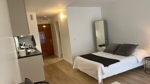 Una habitación pequeña con cama, sofá, una mesita y kitchenette.