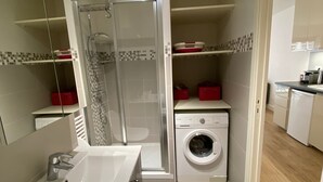Un baño pequeño con ducha, lavabo y lavadora.