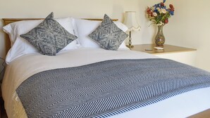 A neatly made bed with patterned pillows, a bedside table with a lamp and a vase of flowers, and a wall art piece. - 3 bedroom accommodation in Ashbourne (Ashbourne)