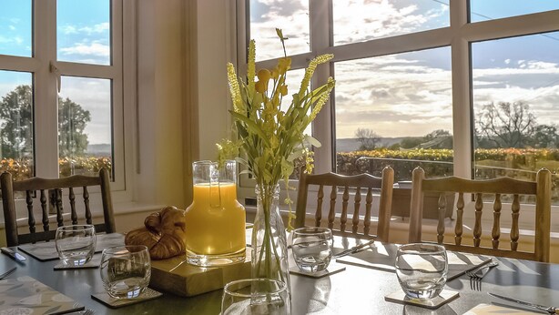 A dining table set with chairs, a vase with flowers, a glass pitcher of orange juice, and a croissant. - 3 bedroom accommodation in Ashbourne (Ashbourne)