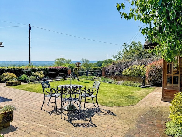 A patio with a round table and chairs, surrounded by a brick pathway and lush greenery. - 3 bedroom accommodation in Ashbourne (Ashbourne)